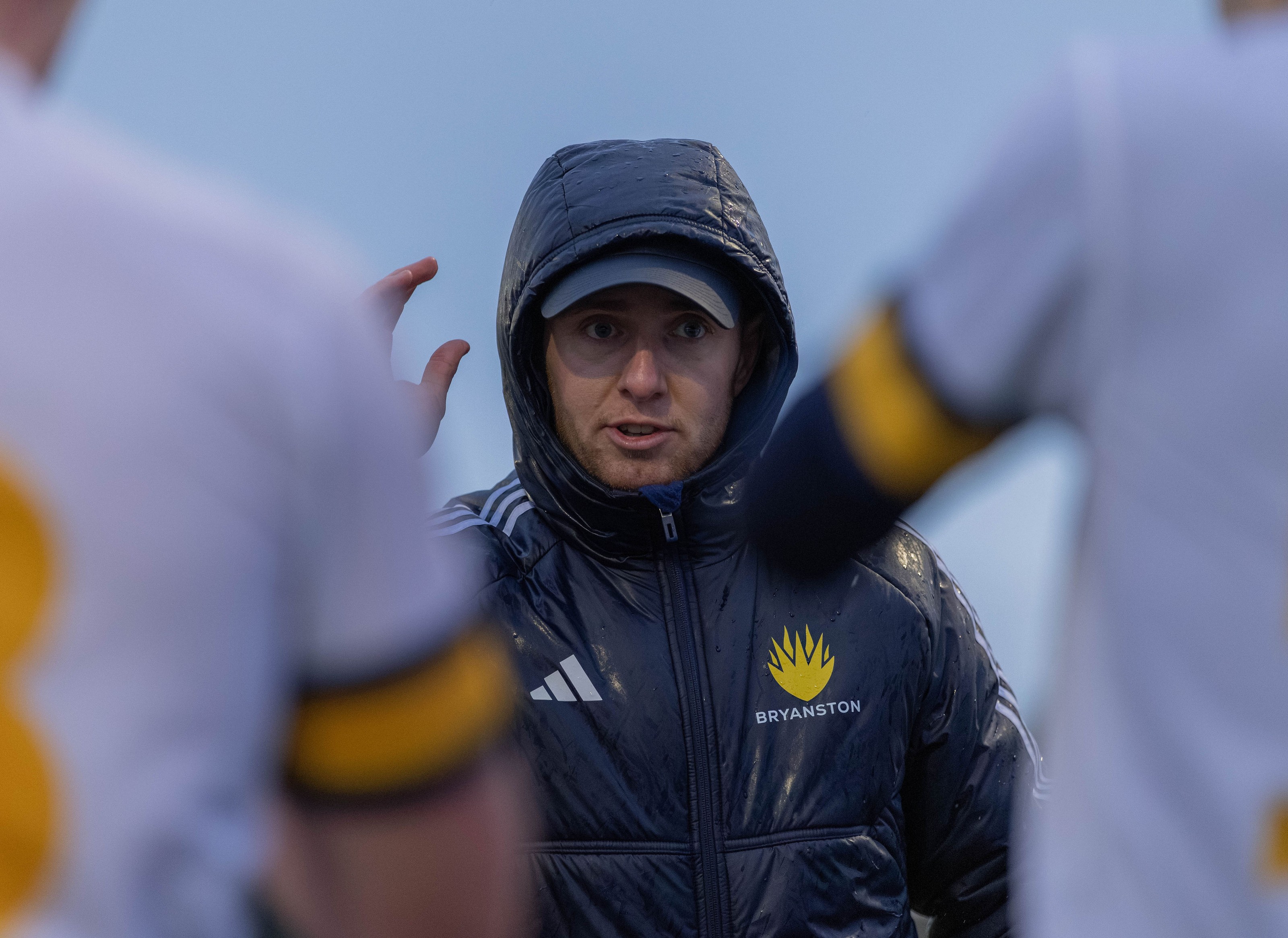 Bryanston coach giving a team talk in the rain, hood up, framed between players