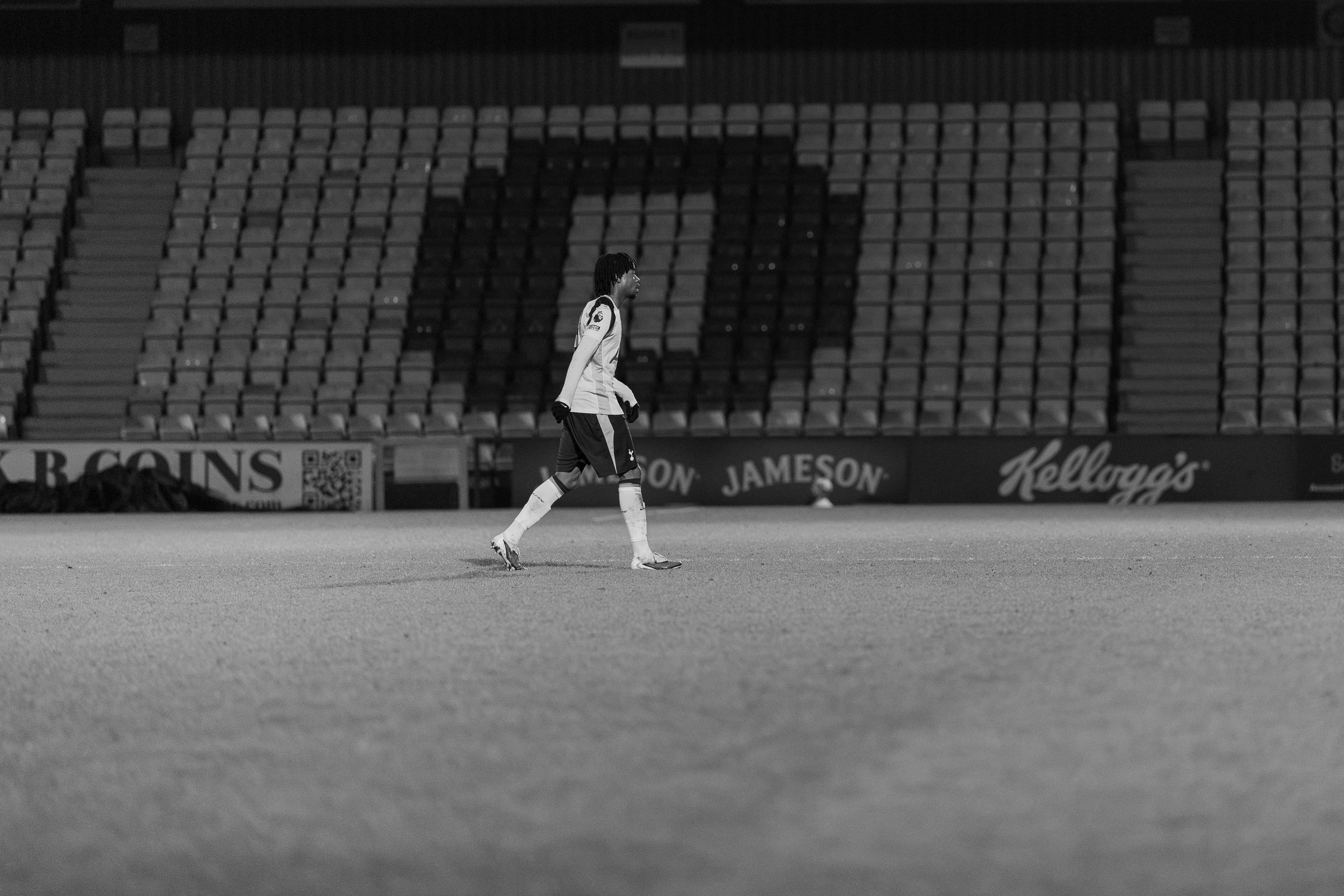 Tottenham U21 player crossing the pitch in front of empty stands, black and white